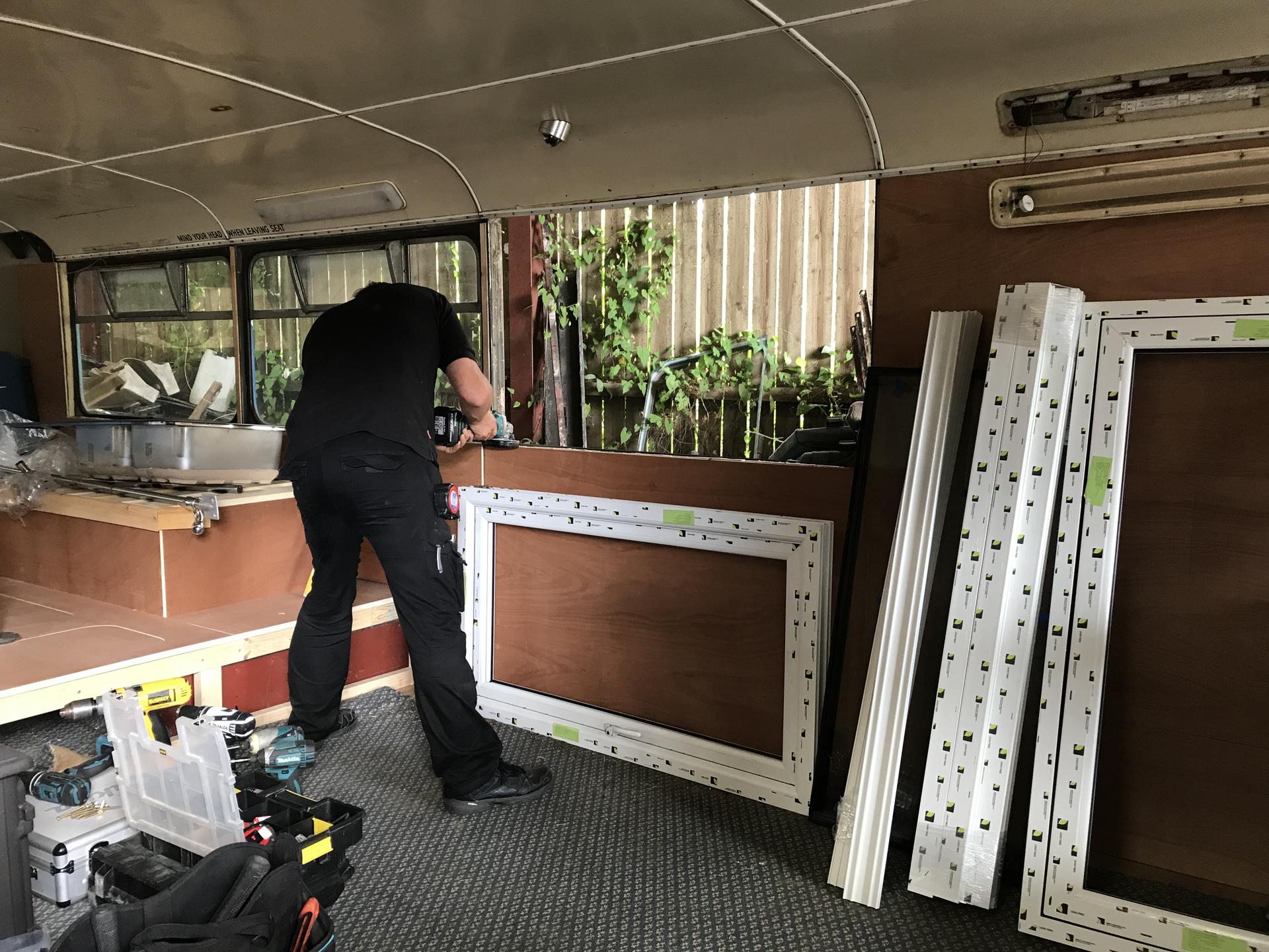 A man in a black shirt installing a Liniar window into the side of a bus