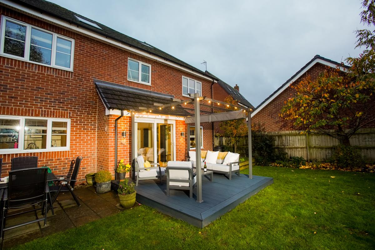 The back garden of a redbrick detached house featuring a patio door leading onto a Liniar SwitchBoard Ultra decking area